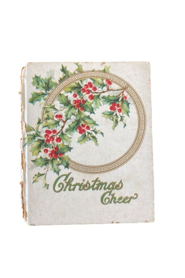 A small white book with illustrated holly with red berries. The title says Christmas Cheer in green lettering.